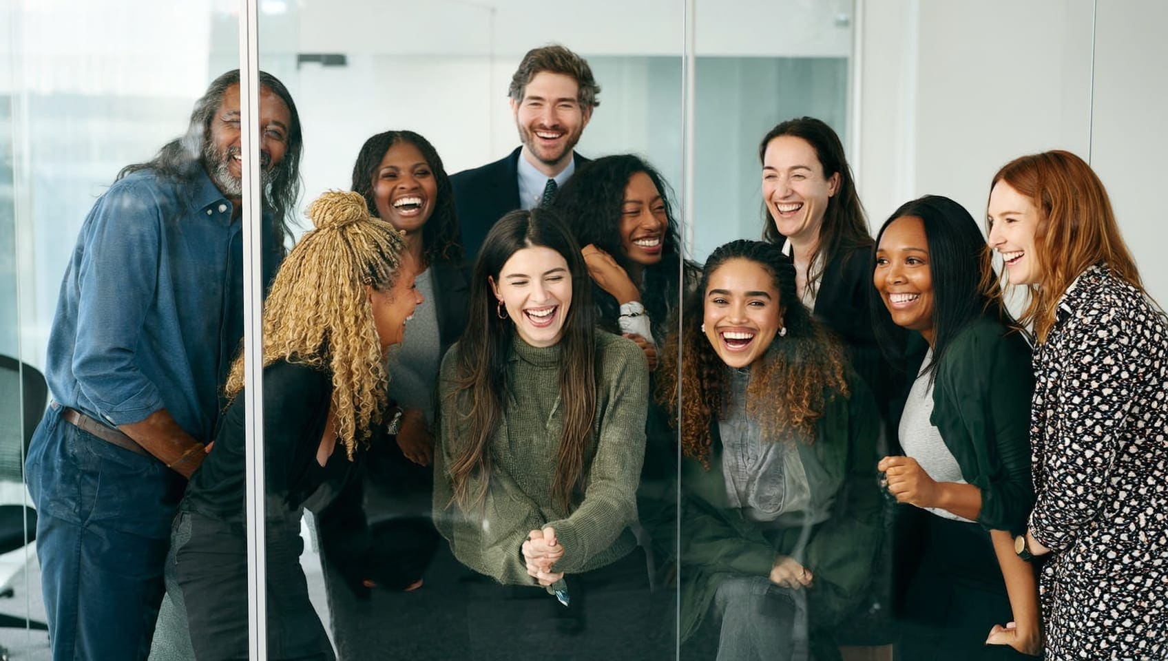 JULY team laughing together beside a glass wall during a working planning session